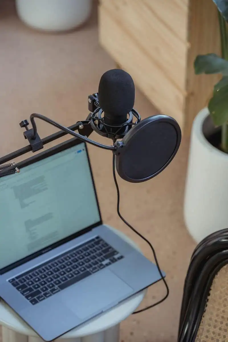 A microphone on a boom arm, a laptop, and headphones on a desk, with no one in the frame